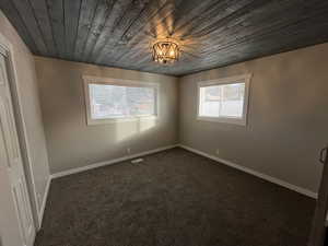 Unfurnished room with wooden ceiling, dark colored carpet, and a chandelier