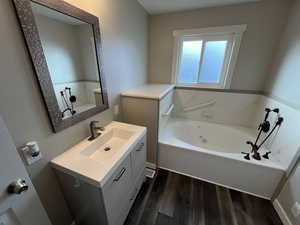 Full bathroom with a jetted tub, vanity, and dark wood-type flooring