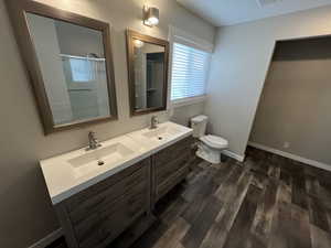 Full bathroom featuring a shower stall, double vanity, and dark wood-style flooring