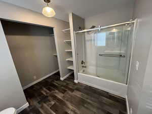 Full bath with dark wood-type flooring and bath / shower combo with glass door
