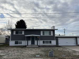 Raised ranch featuring concrete driveway, an attached garage, a chimney, and brick siding