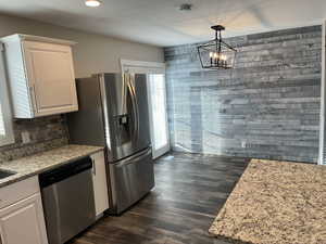 Kitchen featuring dishwasher, light stone countertops, dark wood-style flooring, white cabinetry, and hanging light fixtures