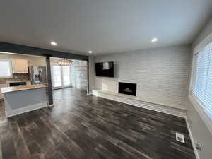 Unfurnished living room with healthy amount of natural light, dark wood-style floors, a fireplace, and recessed lighting