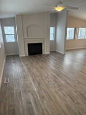 Unfurnished living room with vaulted ceiling, a tiled fireplace, wood finished floors, and ceiling fan