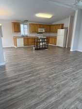 Kitchen with white appliances, brown cabinets, light countertops, open floor plan, and dark wood-type flooring