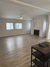 Living room with wood finished floors, a tile fireplace, beam ceiling, and a ceiling fan