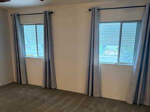 Primary bedroom featuring two large windows, a step-in closet, an en suite bathroom, and a ceiling fan.