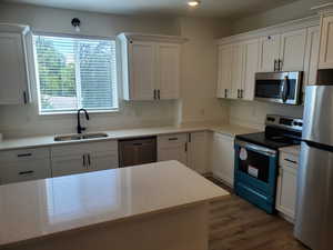 Kitchen with stainless steel appliances, white cabinetry, light stone countertops, and dark wood-style flooring
