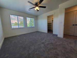 Unfurnished bedroom featuring a spacious closet, dark carpet, and a ceiling fan