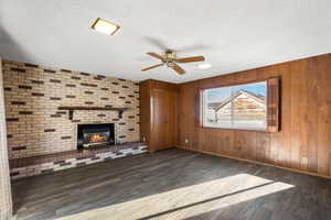 Unfurnished living room featuring wood finished floors, a ceiling fan, a textured ceiling, wood walls, and a fireplace