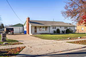 View of front of house with a front lawn, a detached garage, driveway, a chimney, and a porch