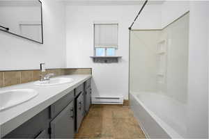 Full bathroom featuring double vanity, bathtub / shower combination, and a baseboard heating unit