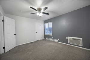 Spare room featuring dark carpet, a baseboard heating unit, a textured ceiling, a wall unit AC, and ceiling fan