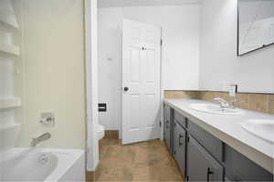 Bathroom with double vanity, bathing tub / shower combination, and stone finish flooring
