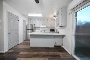 Kitchen with light countertops, a peninsula, appliances with stainless steel finishes, a wall unit AC, and a textured ceiling