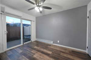 Empty room featuring baseboard heating, a wall mounted AC, dark wood-style flooring, a textured ceiling, and a ceiling fan