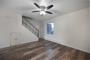 Unfurnished living room featuring a baseboard heating unit, a textured ceiling, stairs, dark wood-style flooring, and a ceiling fan