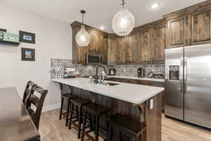 Kitchen featuring appliances with stainless steel finishes, decorative backsplash, decorative light fixtures, a kitchen bar, and a peninsula