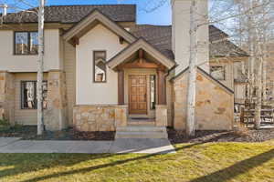 View of front of property with stone siding, a front yard, roof with shingles, stucco siding, and a chimney