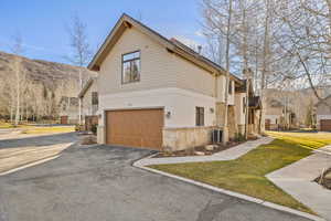 View of home's exterior featuring asphalt driveway, a garage, stone siding, stucco siding, and a yard