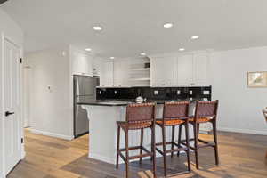 Kitchen featuring a breakfast bar, light wood-style flooring, white cabinets, freestanding refrigerator, and recessed lighting