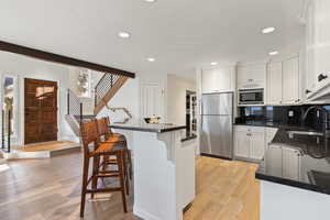 Kitchen with stainless steel appliances, light wood finished floors, a kitchen breakfast bar, white cabinets, and tasteful backsplash