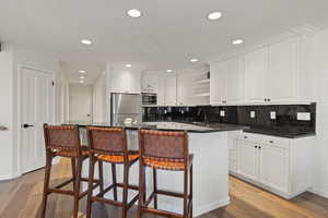 Kitchen with white cabinets, a kitchen bar, stainless steel appliances, open shelves, and decorative backsplash