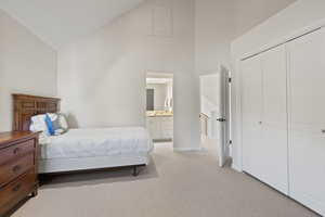 Bedroom with high vaulted ceiling, light colored carpet, a closet, and connected bathroom