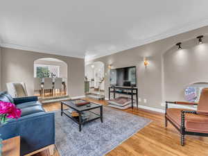 Living area with arched walkways, light wood finished floors, stairs, and ornamental molding