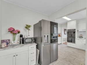 Kitchen with white cabinetry, stainless steel refrigerator with ice dispenser, crown molding, and exhaust hood