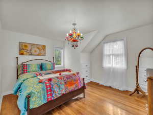 Bedroom with light wood-style flooring, vaulted ceiling, and a chandelier
