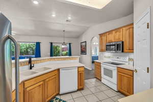 Kitchen with appliances with stainless steel finishes, arched walkways, lofted ceiling, light tile patterned floors, and hanging light fixtures