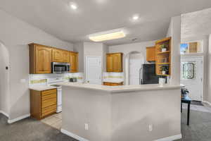 Kitchen with arched walkways, brown cabinets, light countertops, stainless steel appliances, and light tile patterned floors