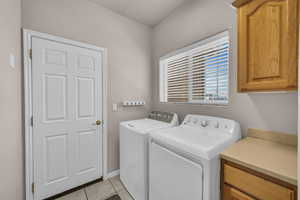 Laundry area with independent washer and dryer, light tile patterned floors, and cabinet space