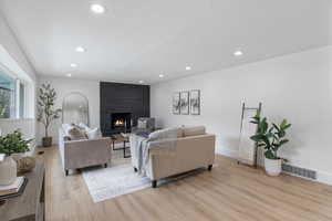 Living area with a large fireplace, light wood-style flooring, recessed lighting, and a textured ceiling