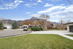 View of green lawn with a mountain view, a garage, and concrete driveway