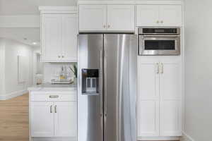 Kitchen featuring stainless steel appliances, white cabinetry, light wood-style floors, and light stone counters