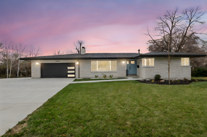 View of front of home featuring brick siding, a chimney, driveway, a front lawn, and a garage