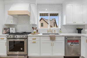 Kitchen with stainless steel appliances, white cabinets, custom exhaust hood, light stone countertops, and tasteful backsplash
