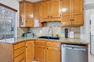 Kitchen with dishwasher, backsplash, light stone countertops, and brown cabinetry