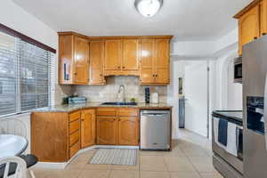 Kitchen with light stone countertops, stainless steel appliances, brown cabinetry, backsplash, and a textured ceiling