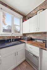 Kitchen with white cabinetry, light wood-type flooring, butcher block countertops, and brick wall