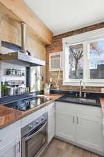 Kitchen featuring wood counters, white cabinetry, stainless steel oven, black electric cooktop, and wall chimney range hood