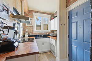 Kitchen featuring butcher block counters, white cabinetry, wall chimney range hood, tasteful backsplash, and light wood-style flooring