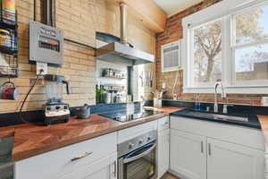 Kitchen featuring wood counters, white cabinets, stainless steel oven, wall chimney exhaust hood, and open shelves