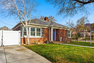 View of front of house featuring brick siding, a chimney, a gate, a front yard, and concrete driveway