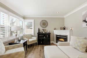 Living area with a glass covered fireplace, ornamental molding, hardwood / wood-style floors, and recessed lighting