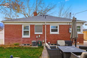 Back of property featuring brick siding, a chimney, a patio area, and a shingled roof