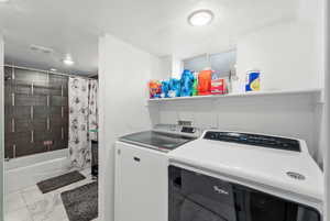 Washroom featuring washing machine and dryer, a textured ceiling, and light marble finish flooring