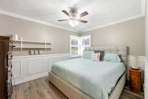 Bedroom with wainscoting, crown molding, a decorative wall, light wood finished floors, and a textured ceiling